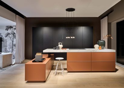 Moderne Häcker Designküche mit Kücheninsel in warmem Orange und schwarzer Rückwand, grifflose Fronten und minimalistische Gestaltung mit edlen Materialien