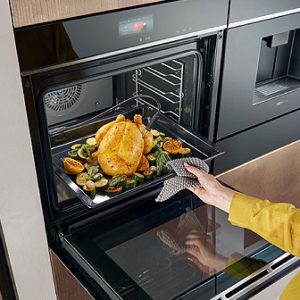 Moderner Siemens Einbaubackofen mit geöffnetem Garraum, zubereitetes Hähnchen auf Backblech, intuitive Touchsteuerung, hochwertige schwarze Glasfront, komfortables und präzises Backen.
