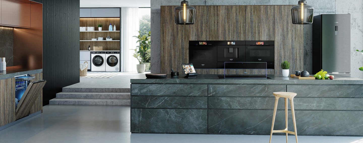 Moderne Designküche mit hochwertigen, integrierten Siemens Einbaugeräte (Backofen, Dampfgarer, Kaffeevollautomat), stilvolle Pendelleuchten und offene Raumgestaltung mit Hauswirtschaftsbereich im Hintergrund